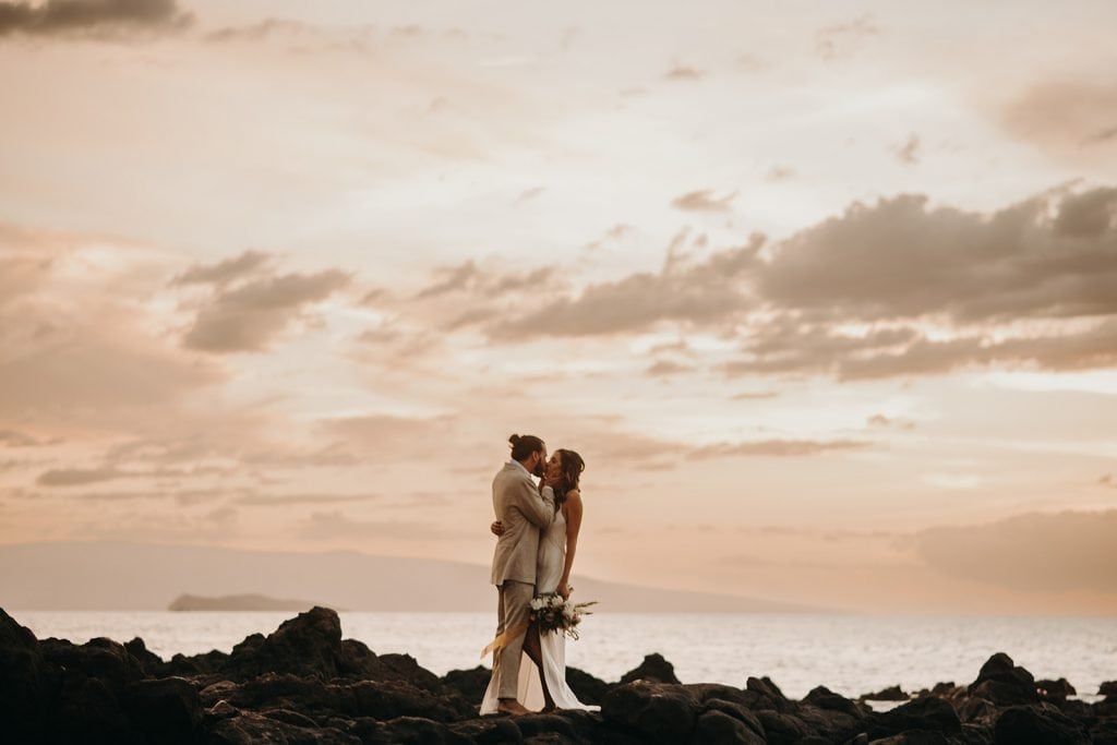 Dana + Josh kissing on rocks at sunset best maui wedding venue