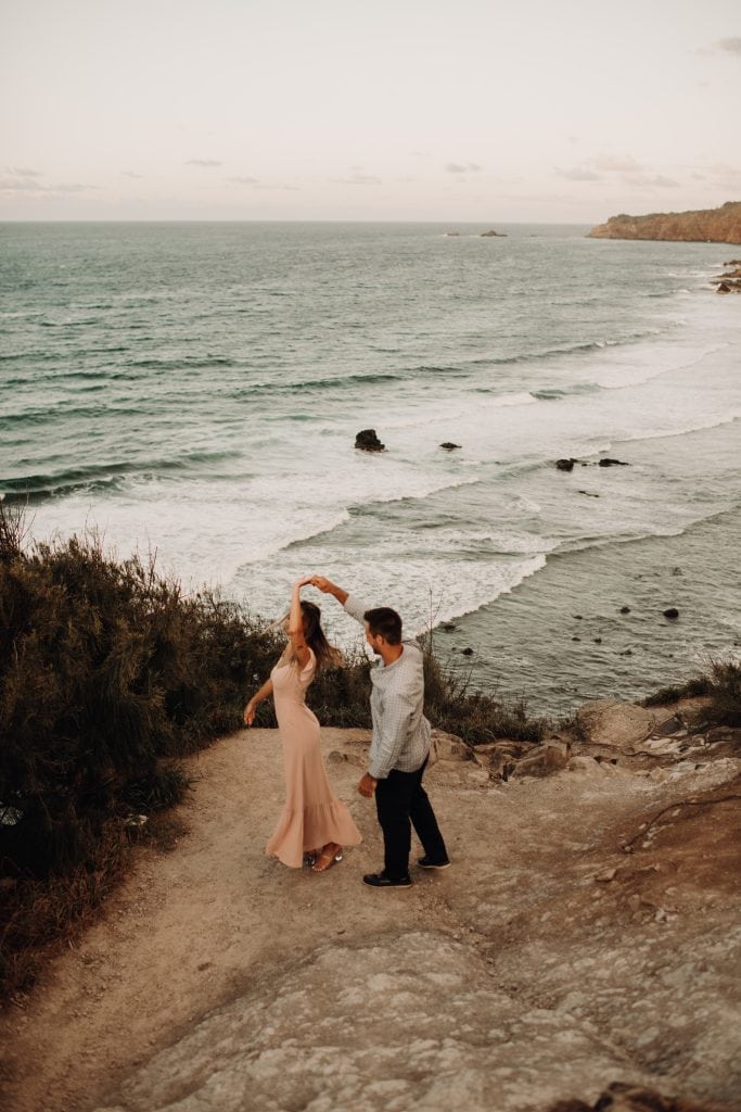 couple dancing on cliff with ocean in background