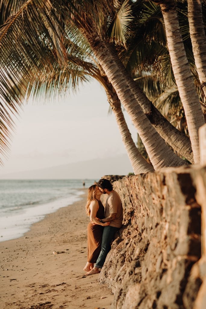 couple leaning against stone wall on the beach while kissing