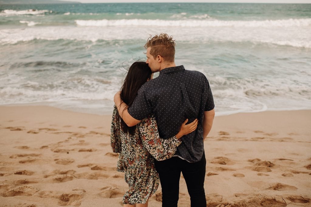 husband kissing wife's forehead on beach
