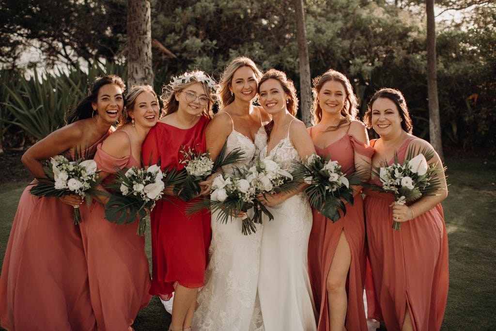 brides with their bridesmaids wearing salmon color bridesmaid dresses holding tropical white floral bouquets