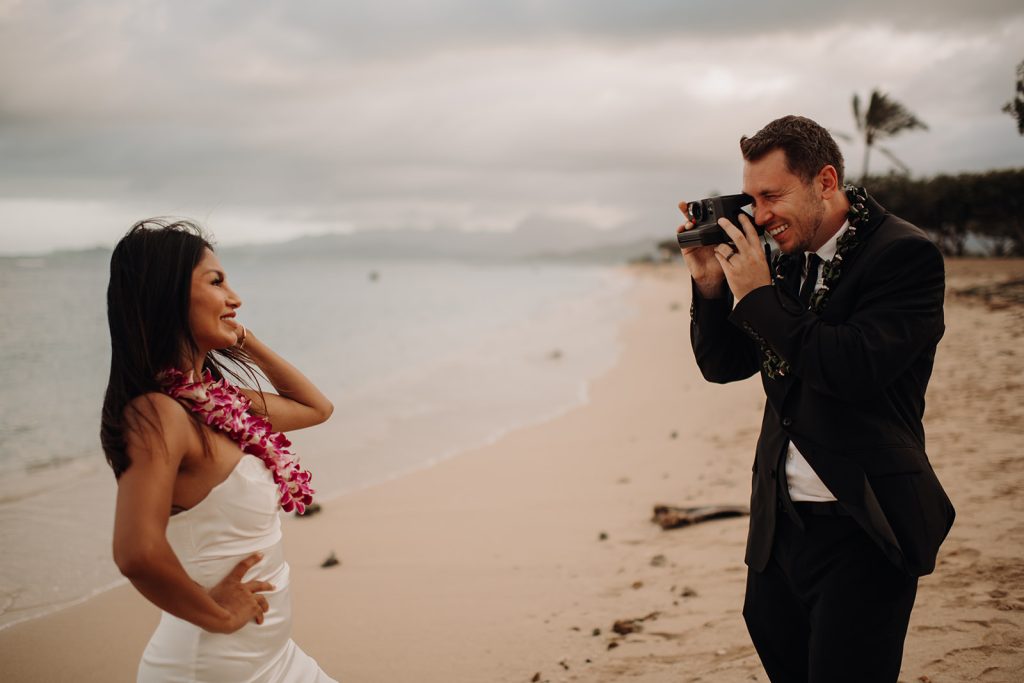 groom taking a photo of the bride with a polaroid camera on the beach