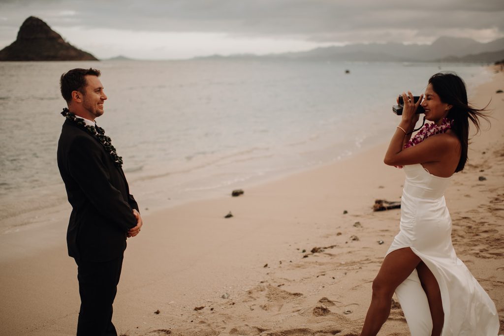 bride taking a photo of the groom with a polaroid camera on the beach