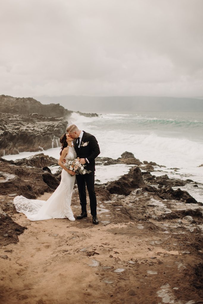 The bride and groom share a kiss with the ocean stretching out endlessly behind them.