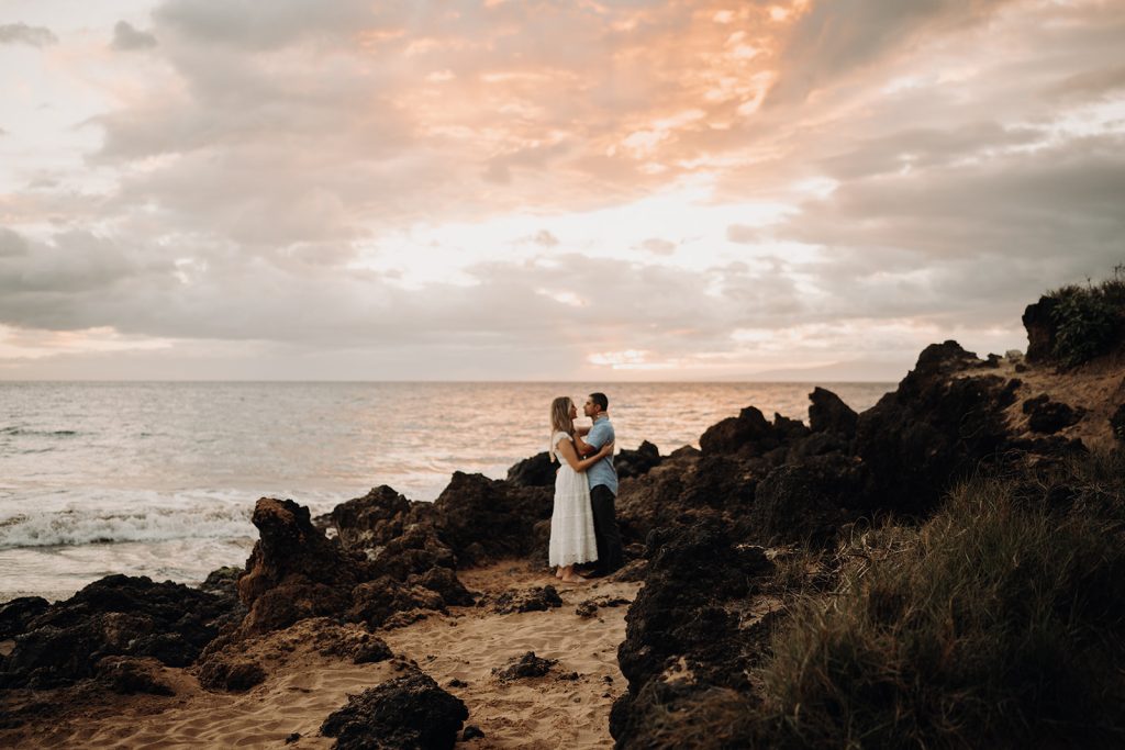 couple standing on lava rocks at sunset