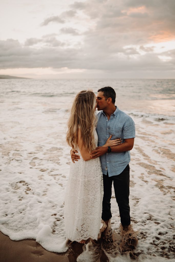 Couple stands in the ocean at sunset