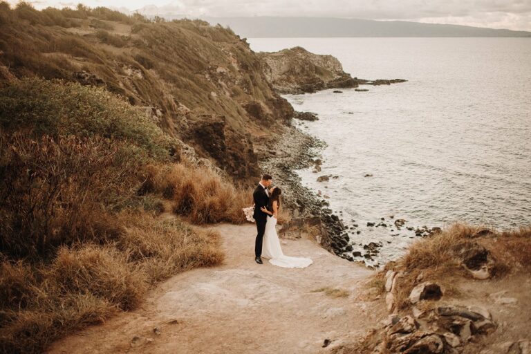 couple hugging on cliff ledge with ocean background